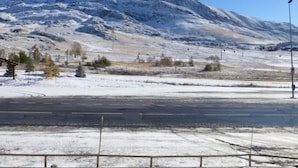 Schneebedeckte Landschaft mit einem Berg im Hintergrund und einer Straße im Vordergrund.
