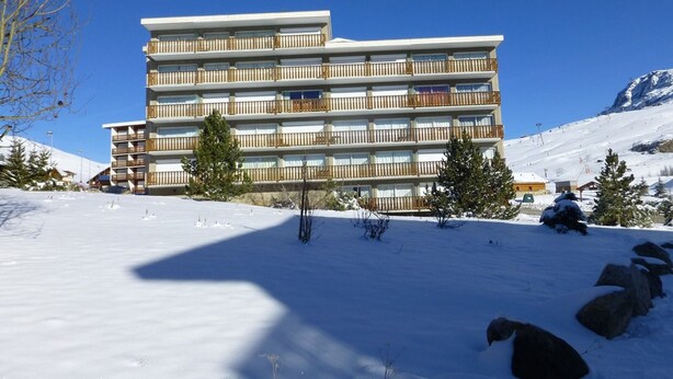 Ein mehrstöckiges Hotel mit Balkonen vor einer verschneiten Berglandschaft.