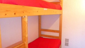 Ein Etagenbett mit roter Bettwäsche in einem Raum mit weißen Wänden und Holzboden.