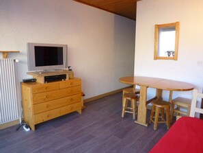 A room with a wooden dresser, a television, a dining table with chairs, and a mirror on the wall.