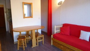 Ein Zimmer mit einem Holztisch, zwei Hockern, einem roten Sofa und einem Spiegel an der Wand.