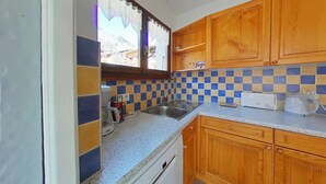 Une cuisine compacte avec des meubles en bois, un pare-feu en carrelage, un lave-vaisselle encastré et une fenêtre avec un rideau.