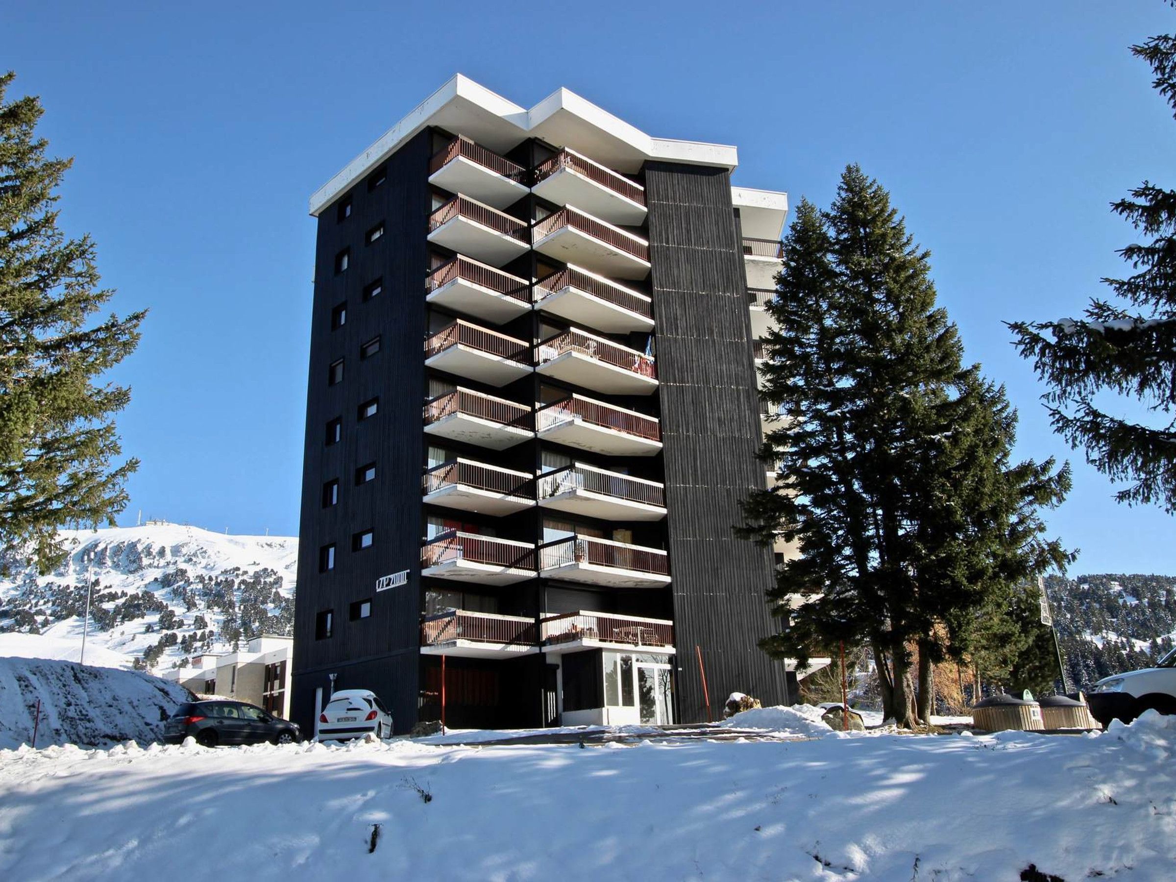 A multi-story building with balconies, surrounded by snow-covered ground and trees.