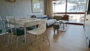 A modern room with a dining table, chairs, a sofa, and a window with a view of a snowy landscape.