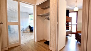 Een kamer met een houten vloer, een bed, een kledingkast en een deur naar een andere kamer.