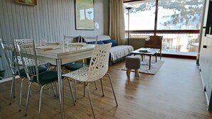 Een moderne kamer met een eettafel, stoelen, een bank en een raam met uitzicht op een besneeerd landschap.