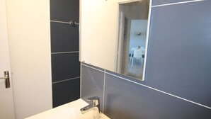 Een badkamer met een wit wastafel, een spiegel en donkere betegelde wanden.