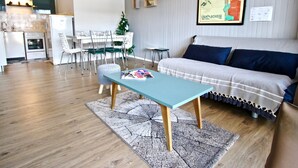 A modern living room with a sofa, a coffee table, and a dining area with chairs and a small table.