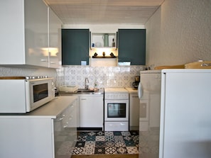 A compact kitchen with white cabinets, a microwave, a stove, and a sink.