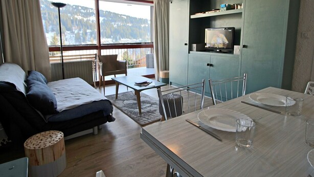 A modern room with a bed, a dining table set for two, a television, and a view of the outdoors.