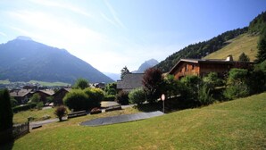 Ein ländliches Haus mit geneigtem Dach, umgeben von einer Rasenfläche und Bäumen.