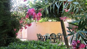Un espacio al aire libre con mesa y sillas, rodeado de abundante follaje y plantas en flor.