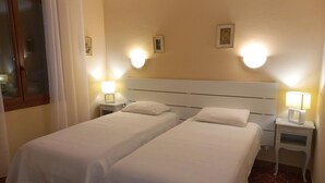 Habitación de hotel con dos camas individuales, una mesita de noche con lámpara y una ventana con cortinas.