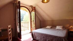 Une chambre à coucher avec un grand lit, une chaise en bois, un bureau et une fenêtre avec une porte ouverte donnant sur l’extérieur.