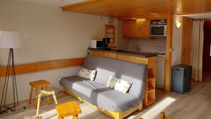 Um espaço de estar compacto com sofá, uma mesinha, luminária, cozinha compacta e um cesto de lixo.