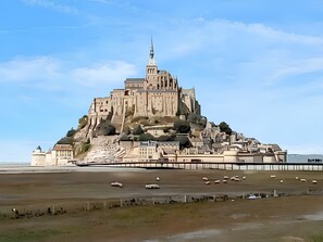 A large, historic castle-like structure with multiple levels and a prominent tower, situated on a hill overlooking a flat landscape with a body of water in the foreground. - Homerez - House near Chanteloup. (Le Pont Cagnon Chanteloup)