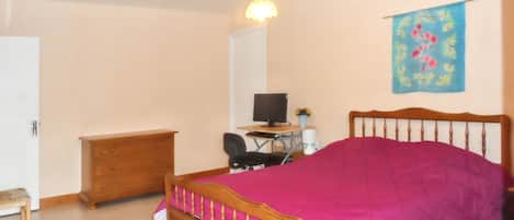 Ein Schlafzimmer mit einem hölzernen Bett, einem Schreibtisch mit Computer, einem Stuhl, einem Kleiderschrank und einer Wandtasche.