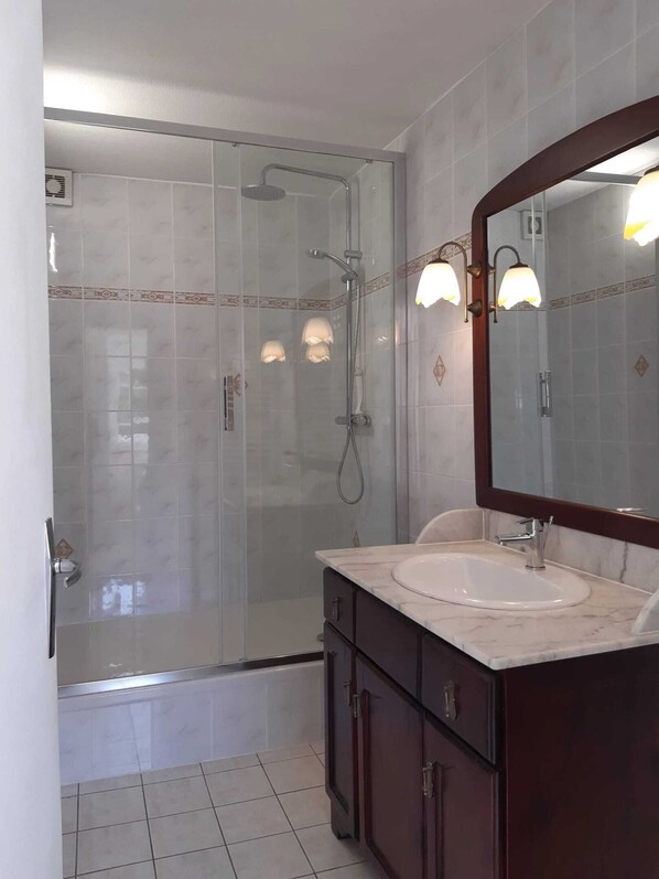 A bathroom with a glass-enclosed shower, a vanity with a sink, and a mirror with wall-mounted lights. - Homerez - House near Chanteloup. (Le Pont Cagnon Chanteloup)