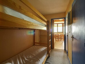 A bunk bed room with a wooden ceiling and a door leading to a dining area.