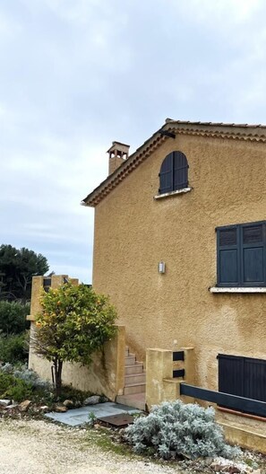 A building with a textured facade, a small arched window, and a door with shutters.