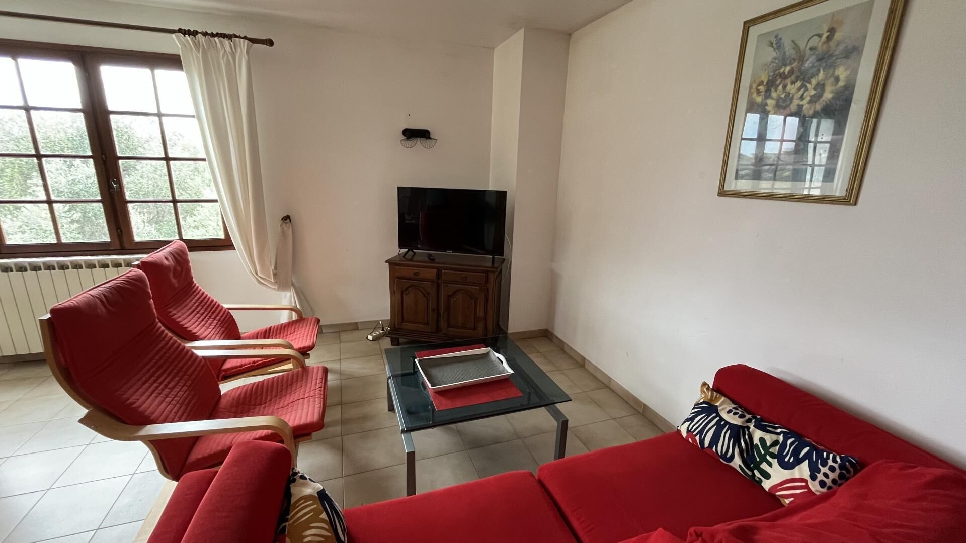 A living room with a sofa, two armchairs, a coffee table, a TV, and a radiator.