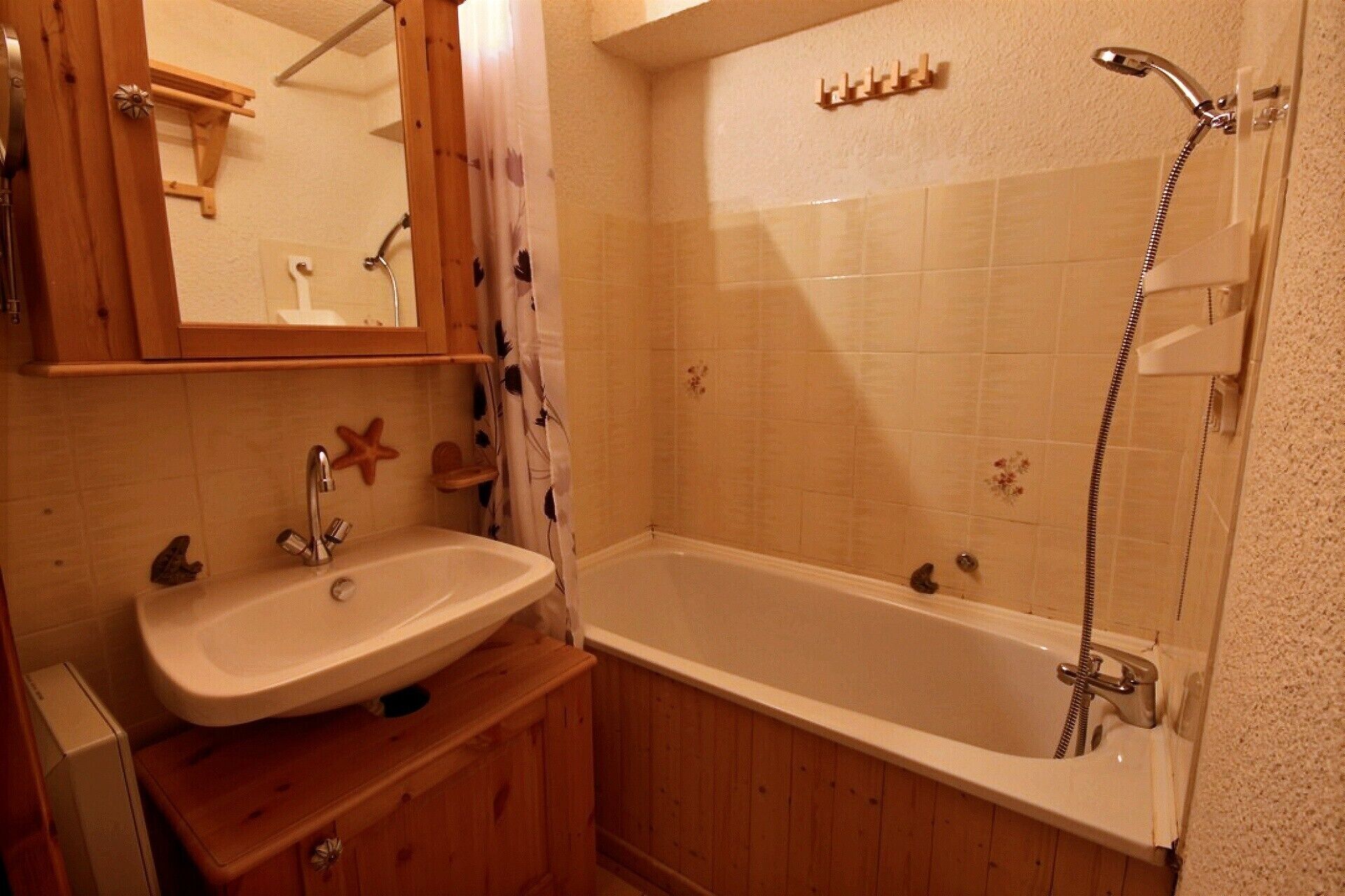 A bathroom with a wooden vanity, a sink, a mirror, and a bathtub with a showerhead.