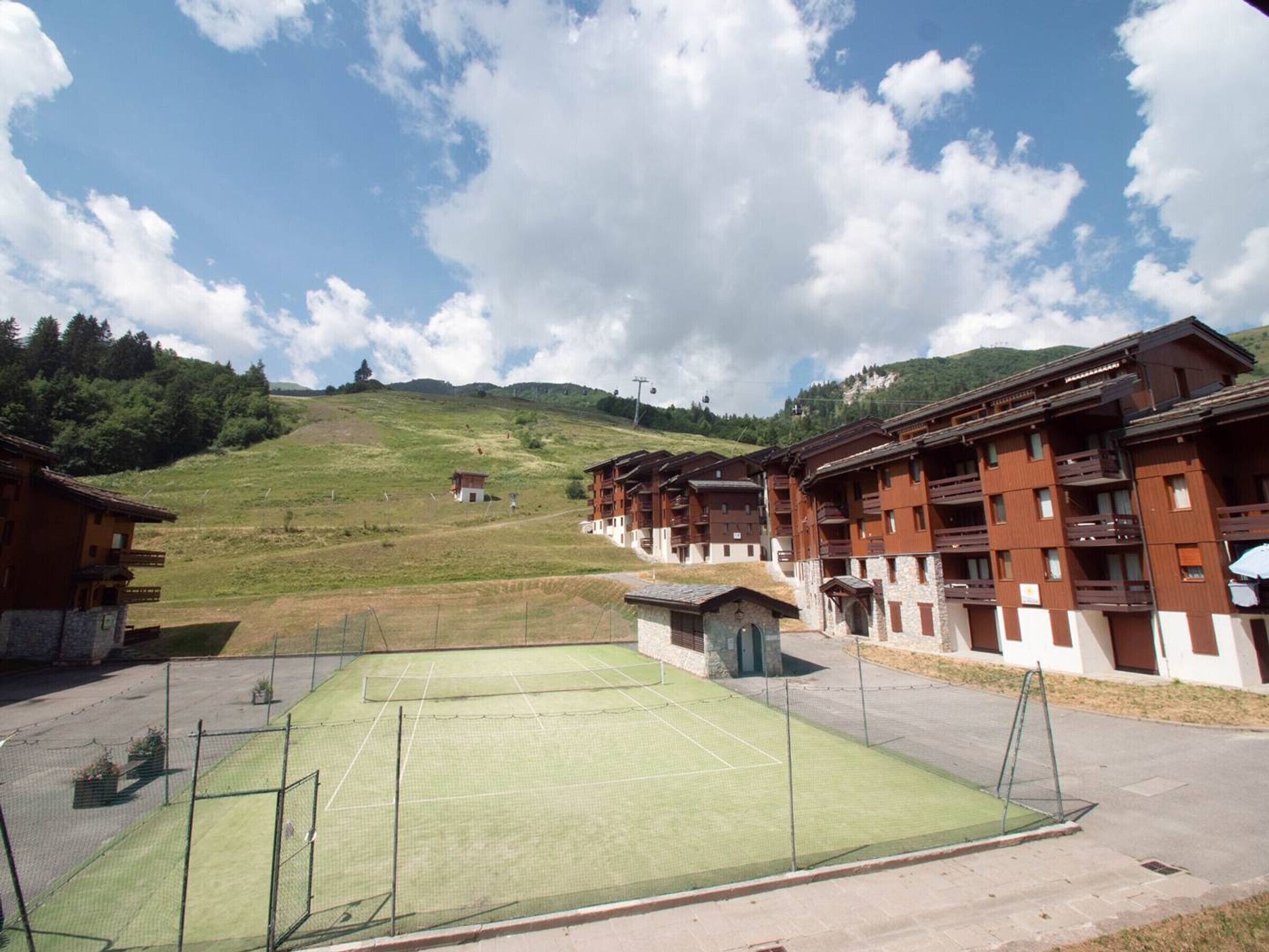 Un court de tennis entouré de bâtiments en bois dotés de balcons, le tout situé dans un paysage vallonné.