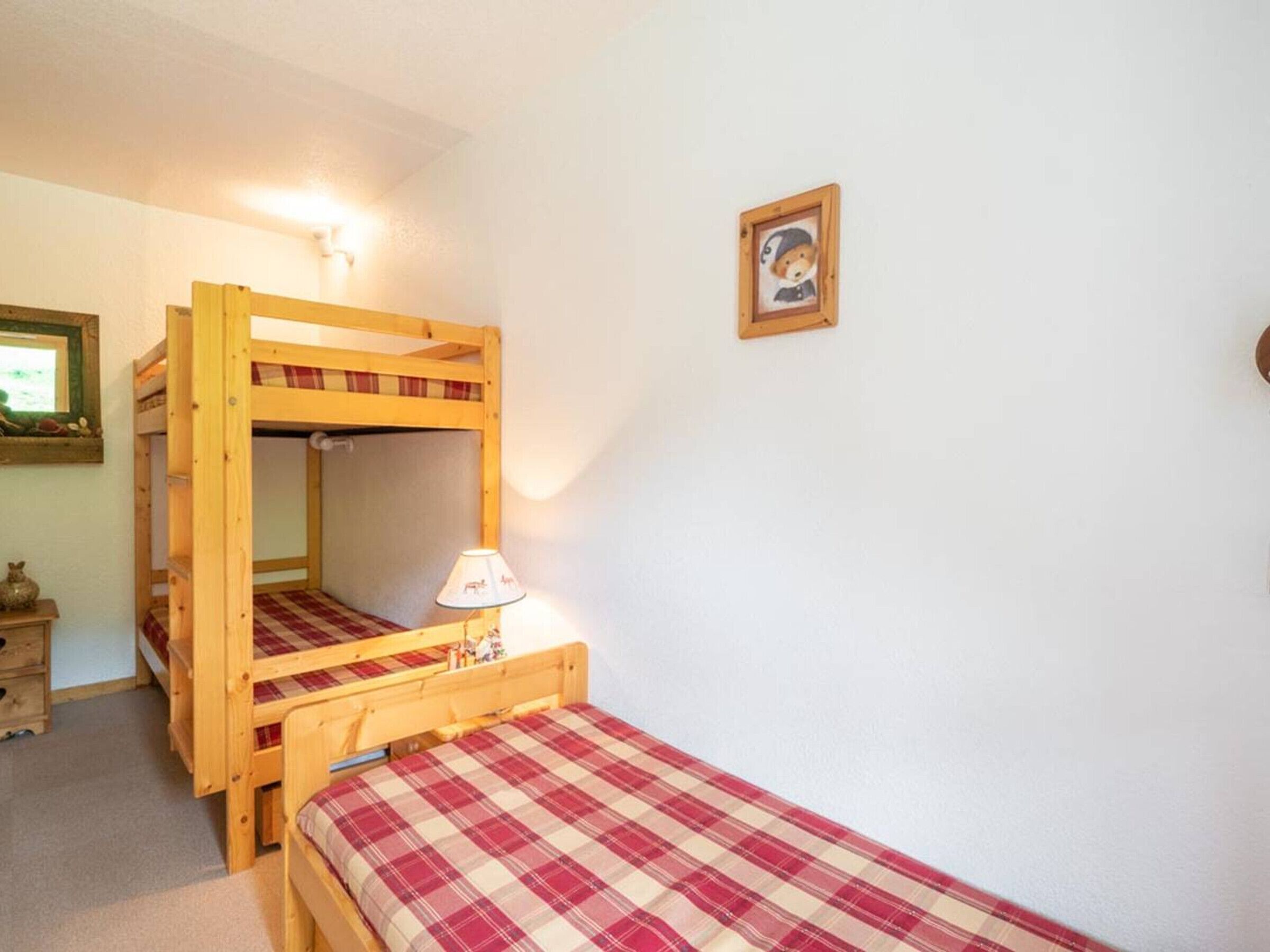 A room with two bunk beds, a small bedside table with a lamp, a framed picture on the wall, and a dresser with a mirror.
