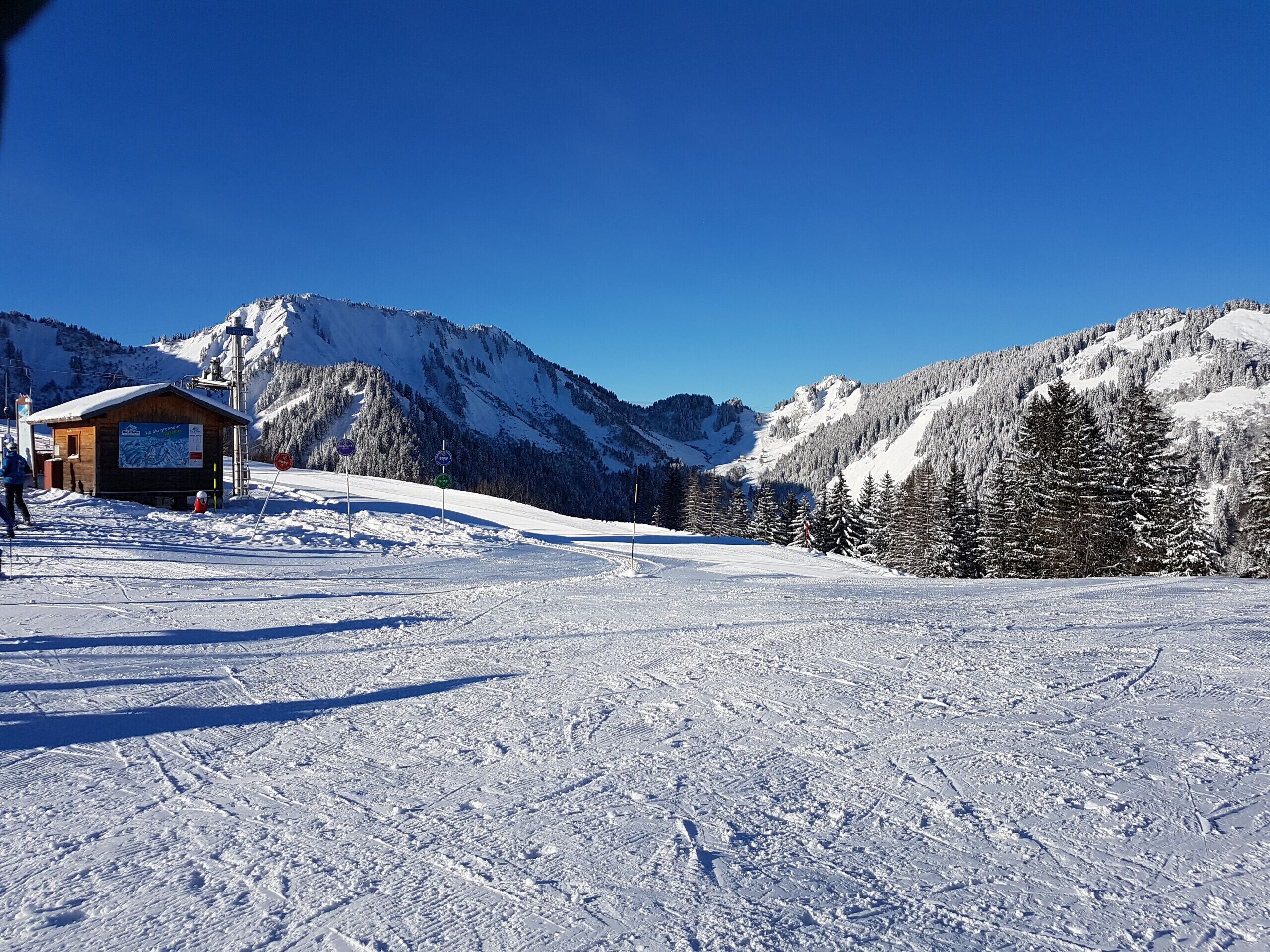 Ein mit Schnee bedeckter Skipisten mit einer Holzhütte und einem Berg im Hintergrund.