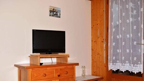 Ein Holzkabinett mit einem Flachbildfernseher darauf, ein kleiner Tisch mit einem Glas und eine Tür mit einem Spitzenvorhang.