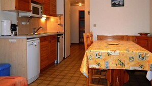 Eine kompakte Küche mit Holzausstattung, einer Mikrowelle und einem Spülbecken. Ein Esstisch mit Stühlen und einer gemusterten Tischdecke ist ebenfalls vorhanden.