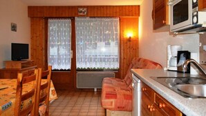 Eine kompakte Küche mit Mikrowelle, Kaffeemaschine und Spüle. Ein Esstisch mit Stühlen und eine Couch sind ebenfalls vorhanden.