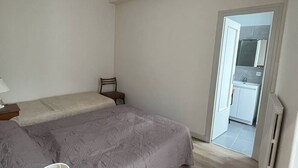 A small, clean room with a bed, a chair, and a small table. There is a door leading to a bathroom with a mirror and sink. - T2 Apartment for 5 in Cauterets (Cauterets)