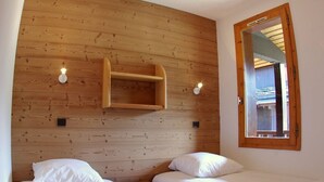 A room with two beds, wooden panel walls, a small shelf, and a mirror. - 2-room apartment in Valmorel with balcony and ski locker (Valmorel)
