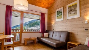 A cozy room with a wooden ceiling, a sofa, a table with chairs, and a window with a mountain view. - 2-room apartment in Valmorel with balcony and ski locker (Valmorel)