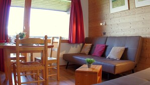 A cozy room with a wooden floor, a sofa, a dining table with chairs, and a window with curtains. - 2-room apartment in Valmorel with balcony and ski locker (Valmorel)