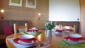 A dining area with a wooden table set for four, two framed pictures on the wall, and a wooden door. - 2-room apartment in Valmorel with balcony and ski locker (Valmorel)