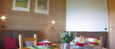 A dining area with a wooden table set for four, two framed pictures on the wall, and a wooden door.