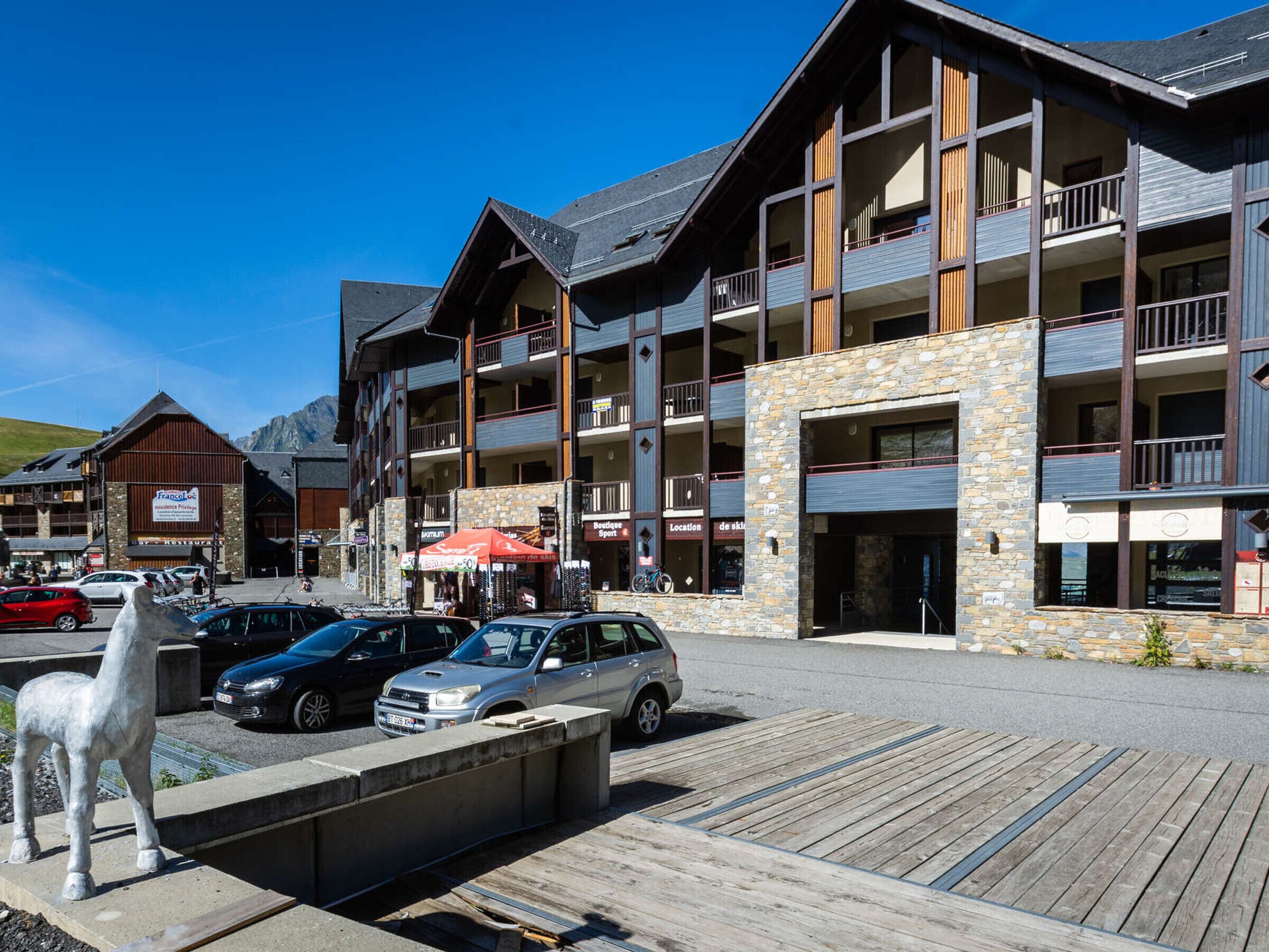 A multi-story hotel with balconies, a stone facade, and a parking area with cars.