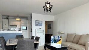 A modern living room with a beige sofa, a dining table with chairs, and a coffee table. There is a kitchen area in the background with white cabinets and a microwave. - 6-sleeper apartment in Banyuls-sur-Mer, air conditioning, parking (Banyuls-sur-Mer)