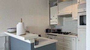 A compact kitchen with white cabinets, a blue countertop, and a small island with a sink. - 6-sleeper apartment in Banyuls-sur-Mer, air conditioning, parking (Banyuls-sur-Mer)