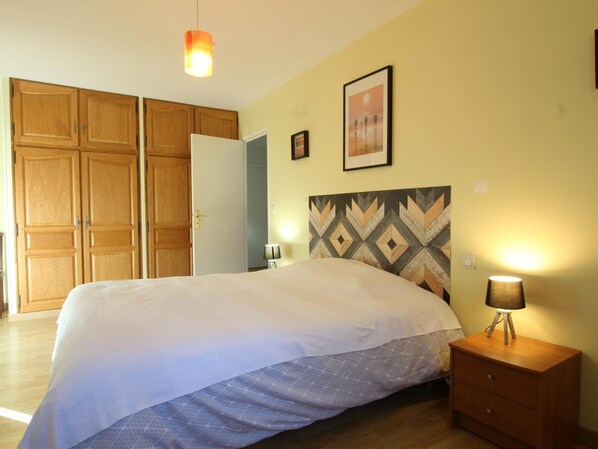 Un dormitorio con cama, armario de madera, lámparas de noche y un cuadro enmarcado en la pared.