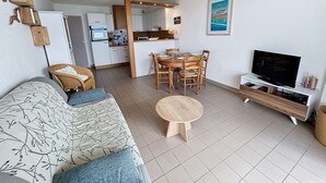 A compact living space with a sofa, dining table, TV, and kitchenette. - Beachfront Apartment with Terrace, Stunning Sea View, Parking & WiFi in Jullouville (Jullouville)
