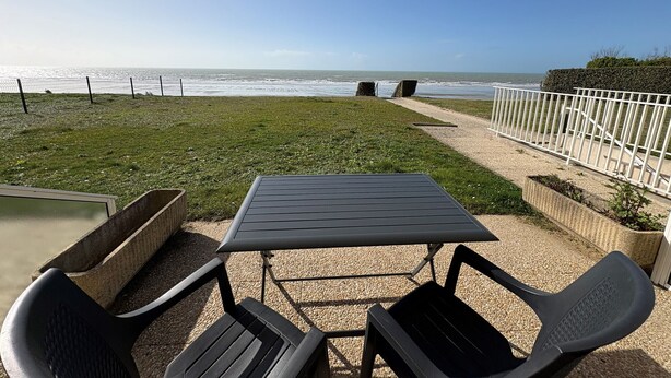 A patio with a table and chairs, a view of the ocean, and a white fence. - Beachfront Apartment with Terrace, Stunning Sea View, Parking & WiFi in Jullouville (Jullouville)