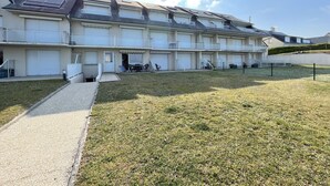 A multi-story residential building with a flat roof, large windows, and a grassy courtyard. - Beachfront Apartment with Terrace, Stunning Sea View, Parking & WiFi in Jullouville (Jullouville)