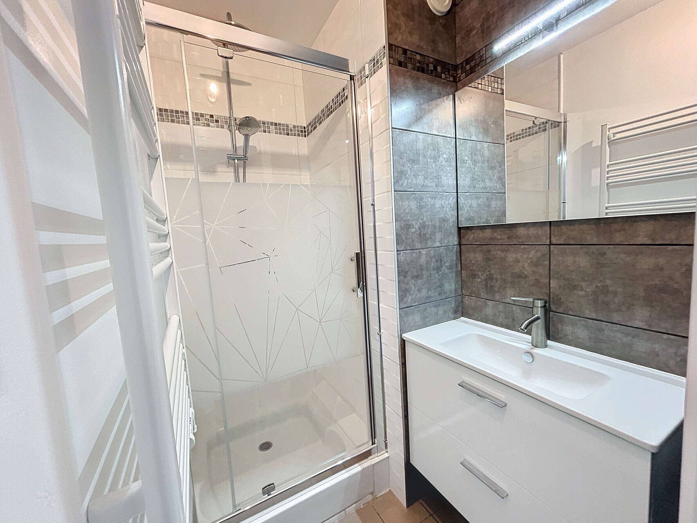 Une salle de bain moderne avec une douche à parois de verre, un lavabo blanc et un mur recouvert de carreaux.