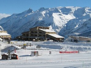Une station de montagne enneigée, avec un grand bâtiment doté de nombreux balcons, de remontées mécaniques et d’une piste de ski.