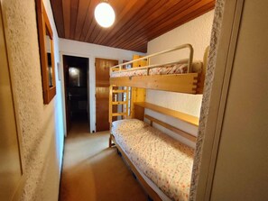 A narrow hallway with a bunk bed on the right, a wooden ceiling, and a door leading to another room.