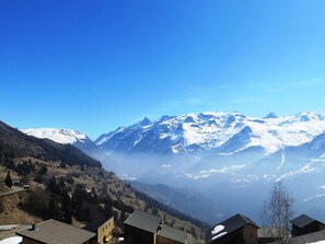 Un village de montagne aux sommets enneigés, aux maisons aux toits inclinés et sous un ciel bleu azur.