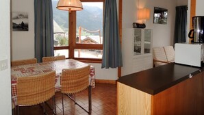 Un'accogliente cucina con un bancone in legno, un tavolo da pranzo con sedie in vimini e vista sulle montagne dalla finestra.